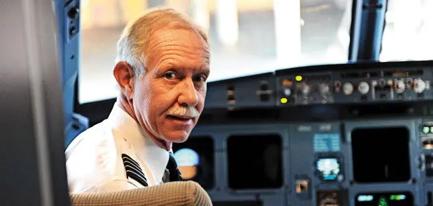 Captain Chesley 'Sully' Sullenberger in uniform, seated in an aircraft cockpit and looking back over his shoulder.