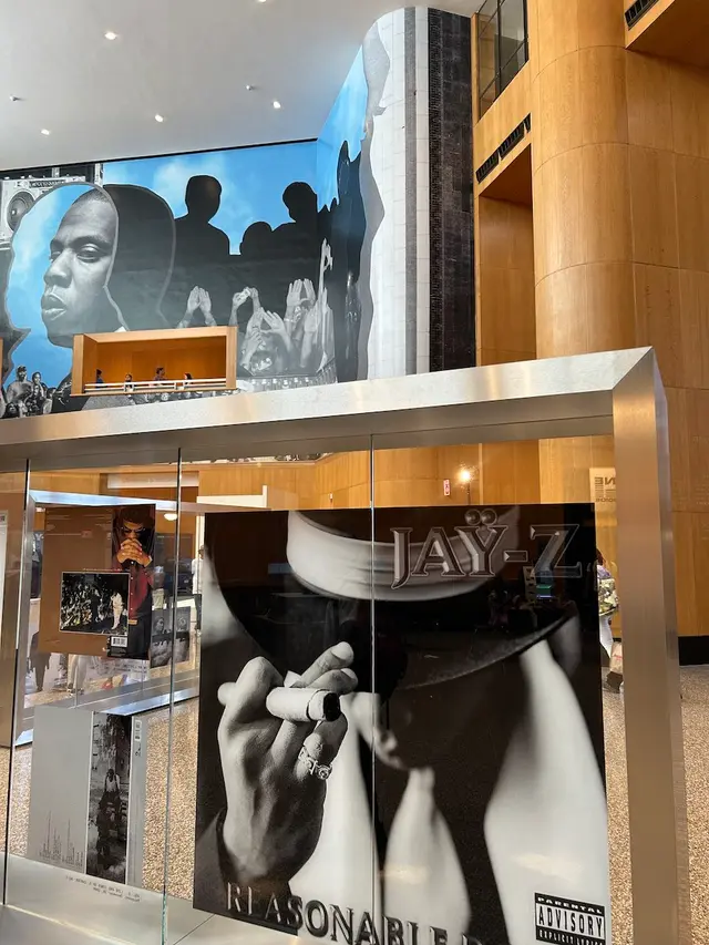 Jay-Z exhibition entrance with a large mural of a face and raised hands above a glass case showing an album cover
