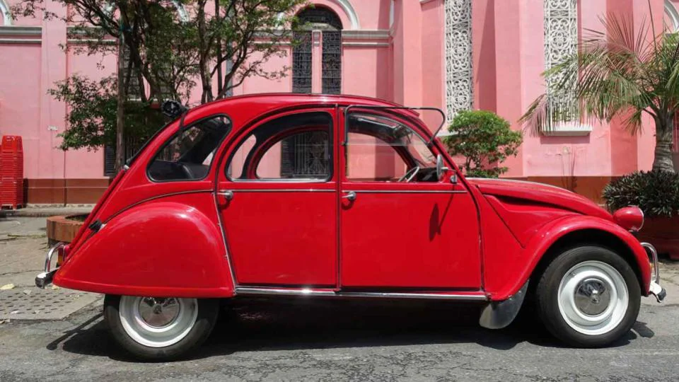 Slide with a red vintage car parked in front of a pink building, used as a visual in the talk