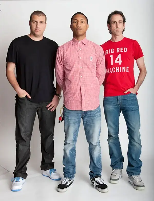 Three men standing in a studio, in a black t-shirt, a pink checked shirt, and a red Big Red Machine t-shirt