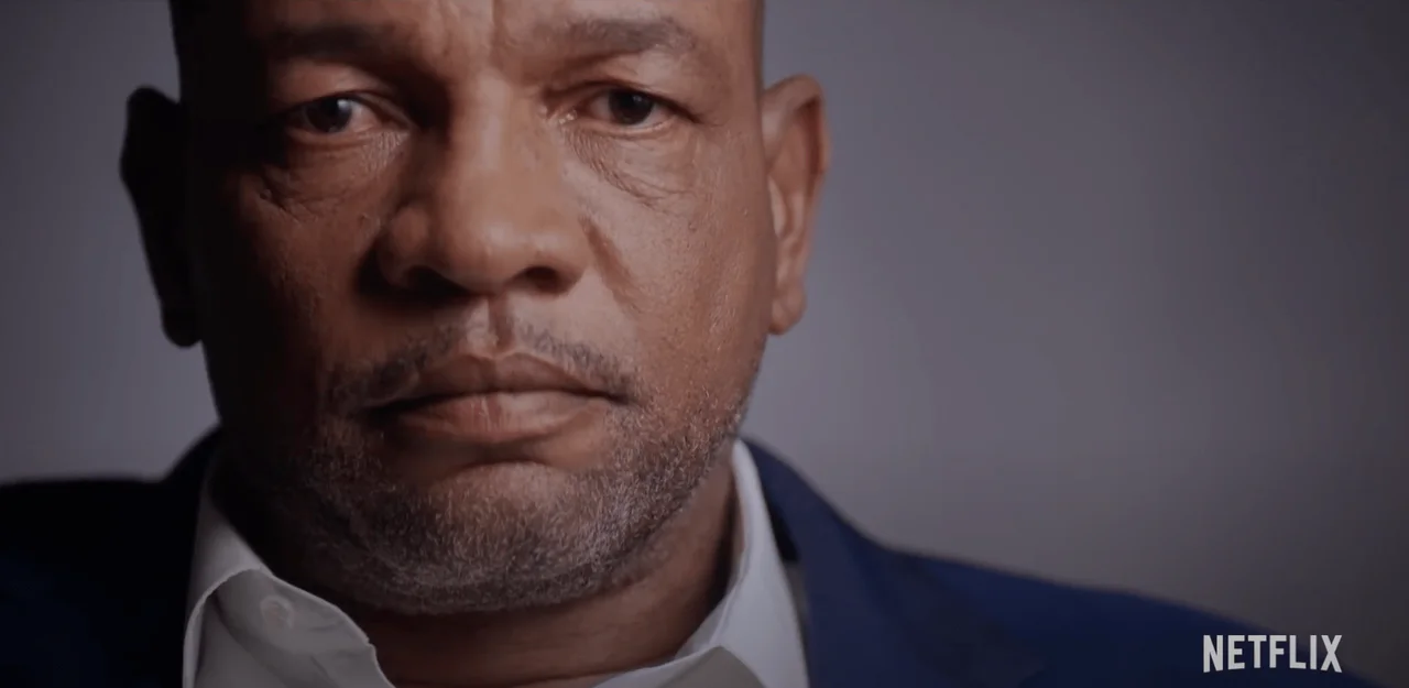Close-up of a serious man's face in a blue jacket, a still from the Netflix documentary series