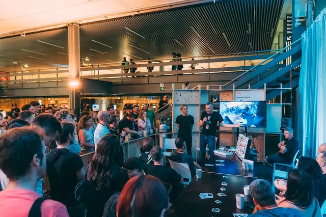 Crowd gathered around a speaker with a microphone, presenting a modular synth demo on a screen at a festival