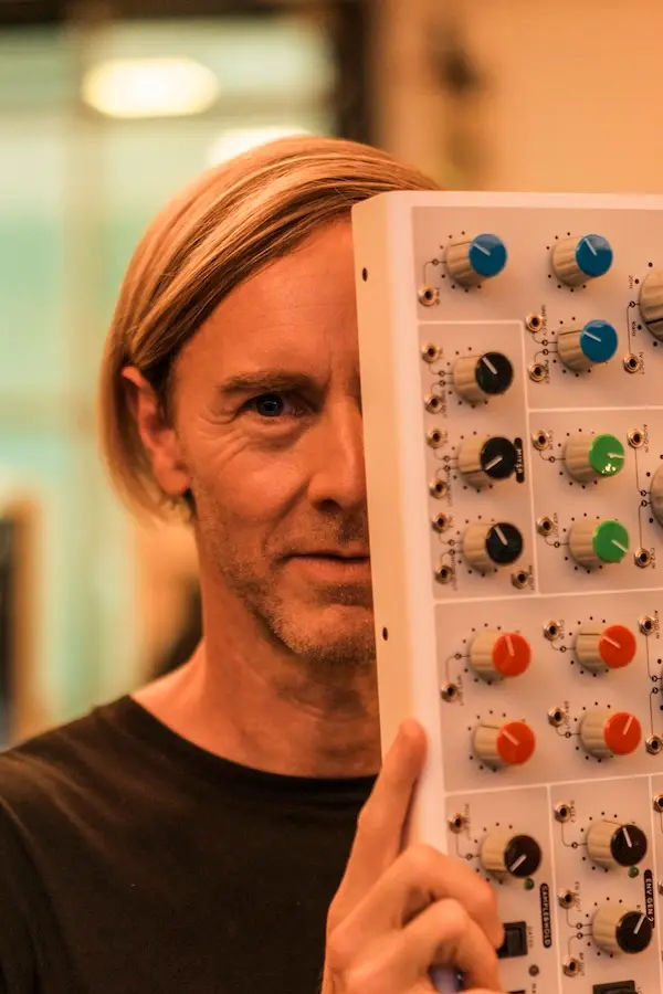 Man smiling from behind a Bullfrog synth, holding it up so it covers half his face