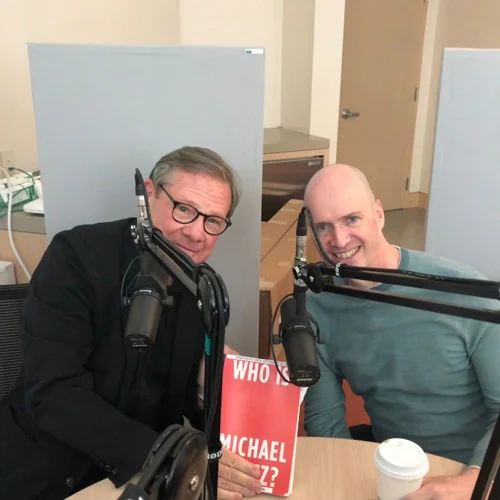 Michael Ovitz and Ben Horowitz leaning toward each other at podcast microphones, with a book on the table