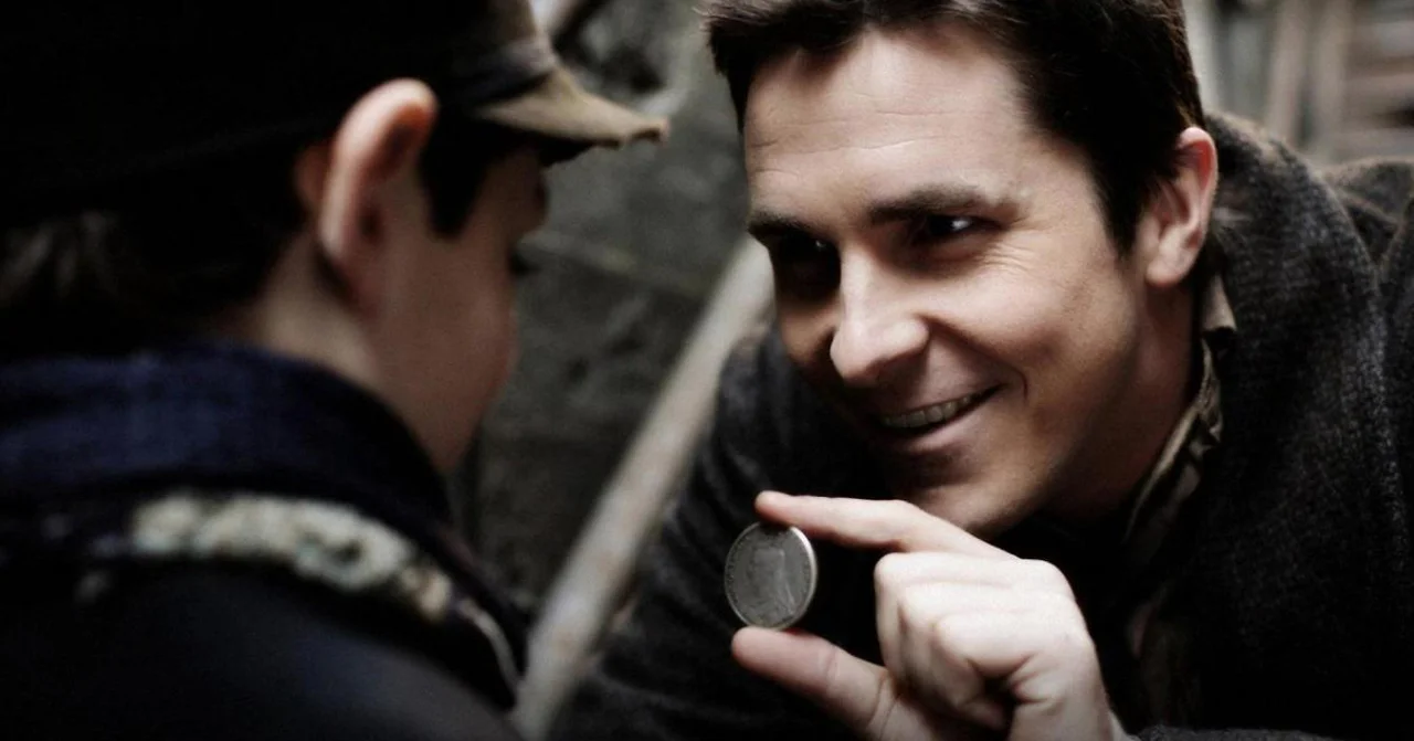 Film still of Christian Bale as Alfred Borden, smiling and holding up a coin to a boy