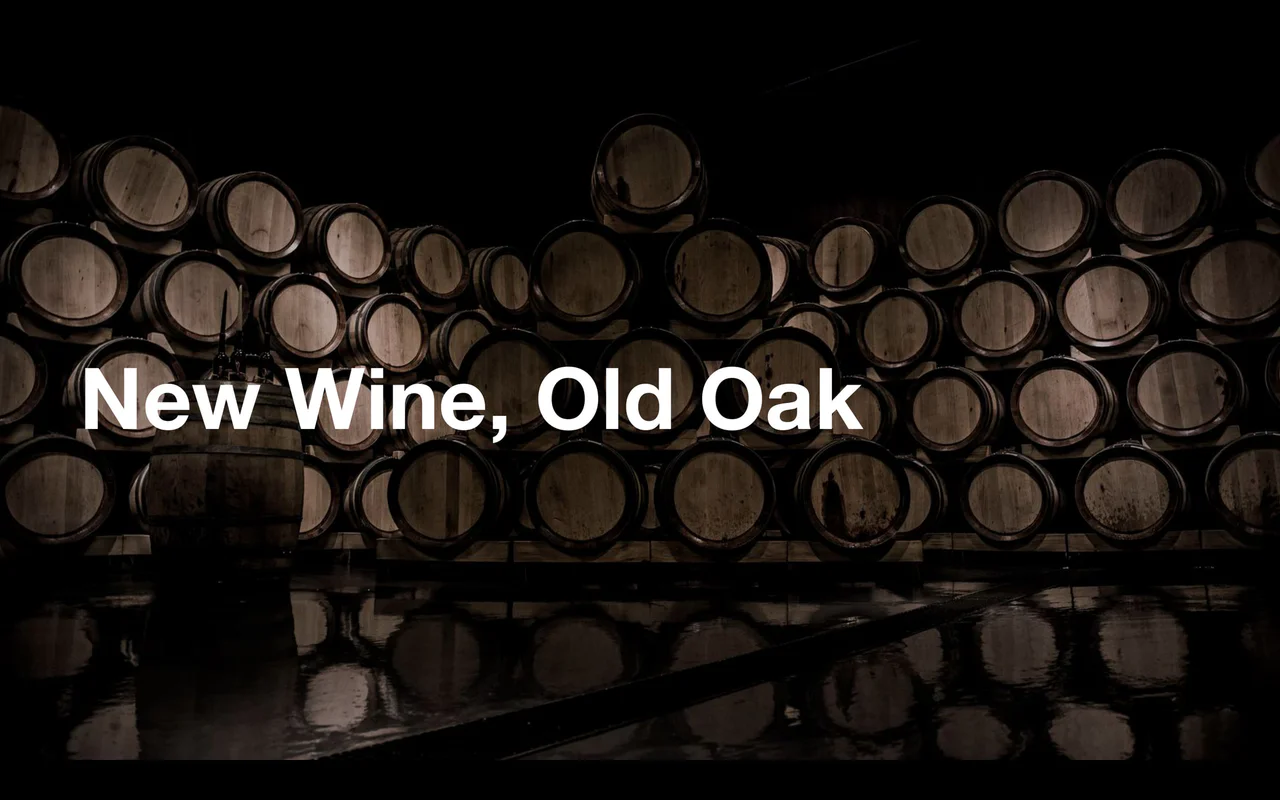 A cellar of oak barrels in low light, with the words New Wine, Old Oak.