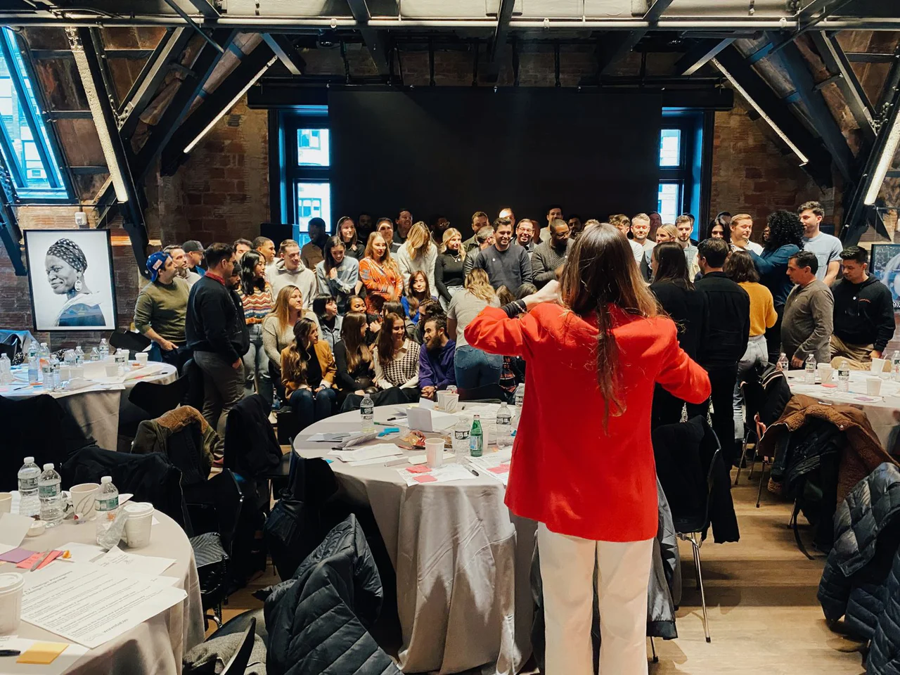 The Wasserman team gathered at the front of a brick-walled hall with round tables, seen from behind a host in a red jacket
