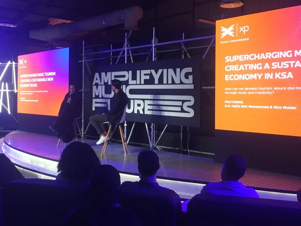 The XP stage, lit blue and orange, with the words Amplifying Music Futures behind two speakers and an audience in silhouette